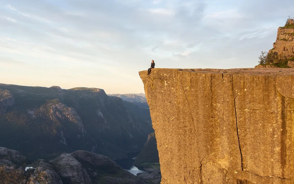 A hiker sits on the edge of the flat Preikestolen rock in low morning light