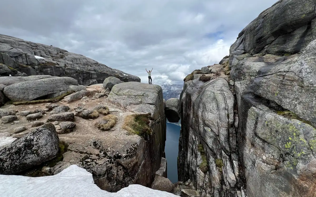 A hiker with raised arms on a rounded rock between two granite walls