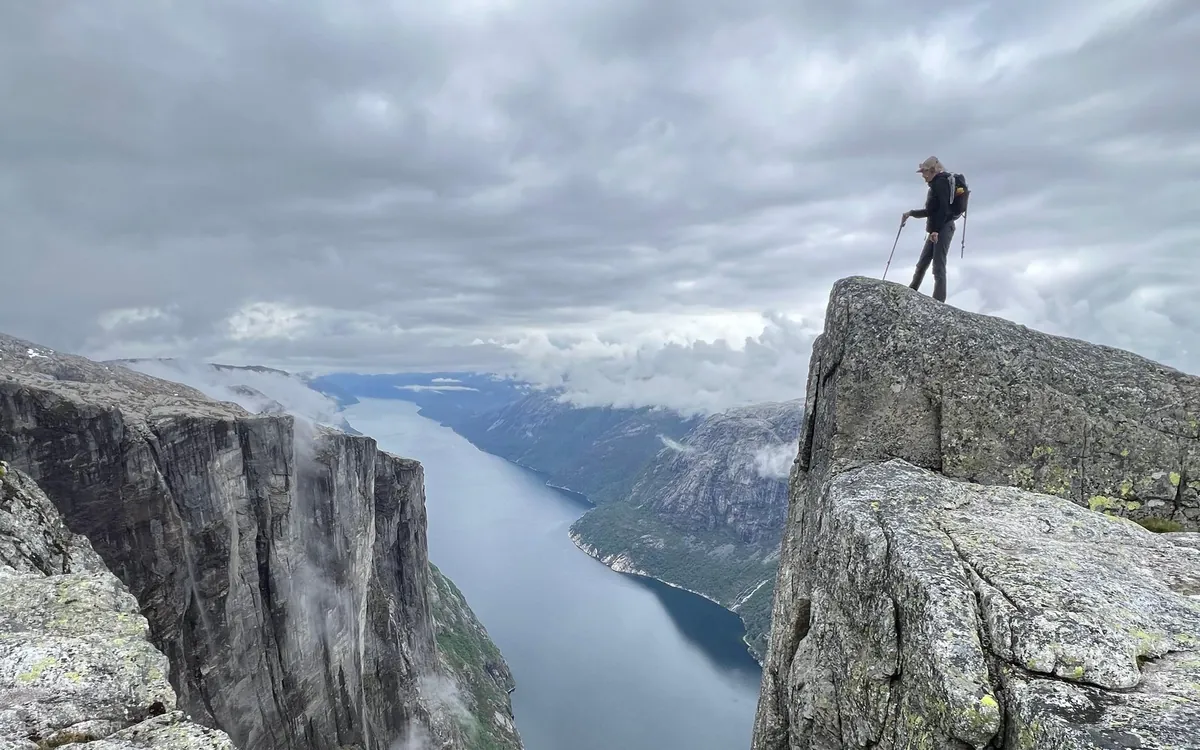 A hiker standing on a rocky ledge high above a fjord