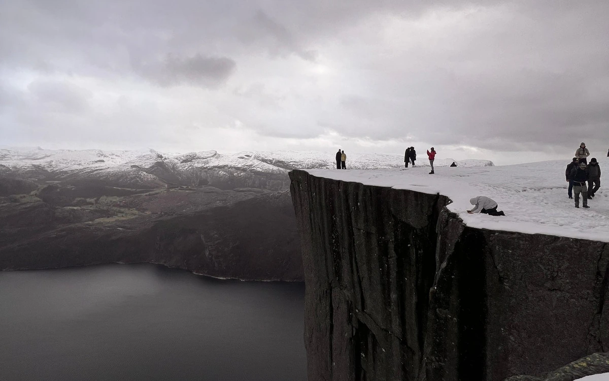 Hikers on a snow-covered clifftop under a grey sky