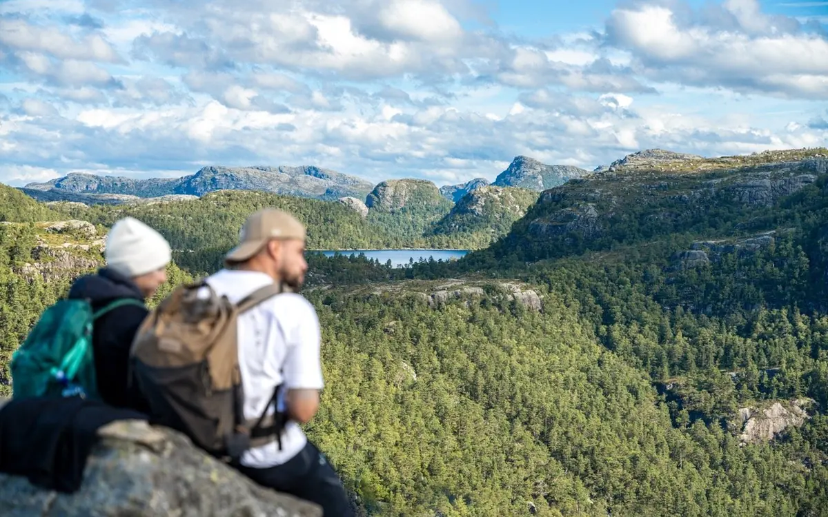 Two hikers with daypacks resting on a rock above a forested valley and a lake