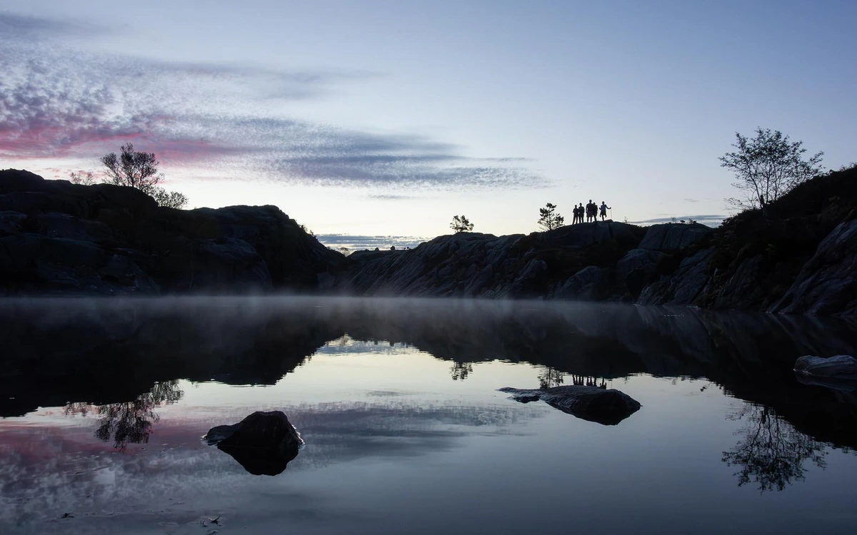 Mist over a still mountain lake with a small group on the ridge above