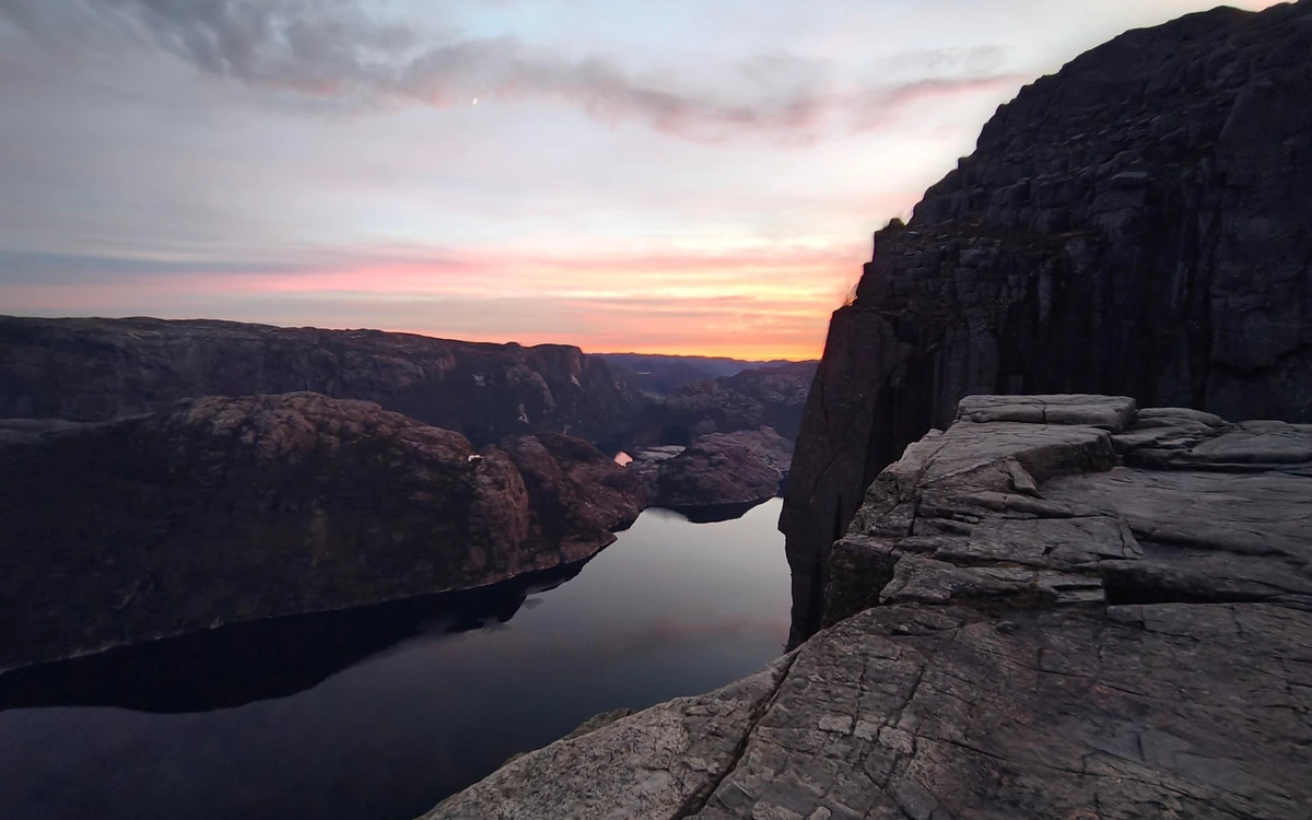 Cracked granite at the cliff edge with the fjord far below under a cloudy sky