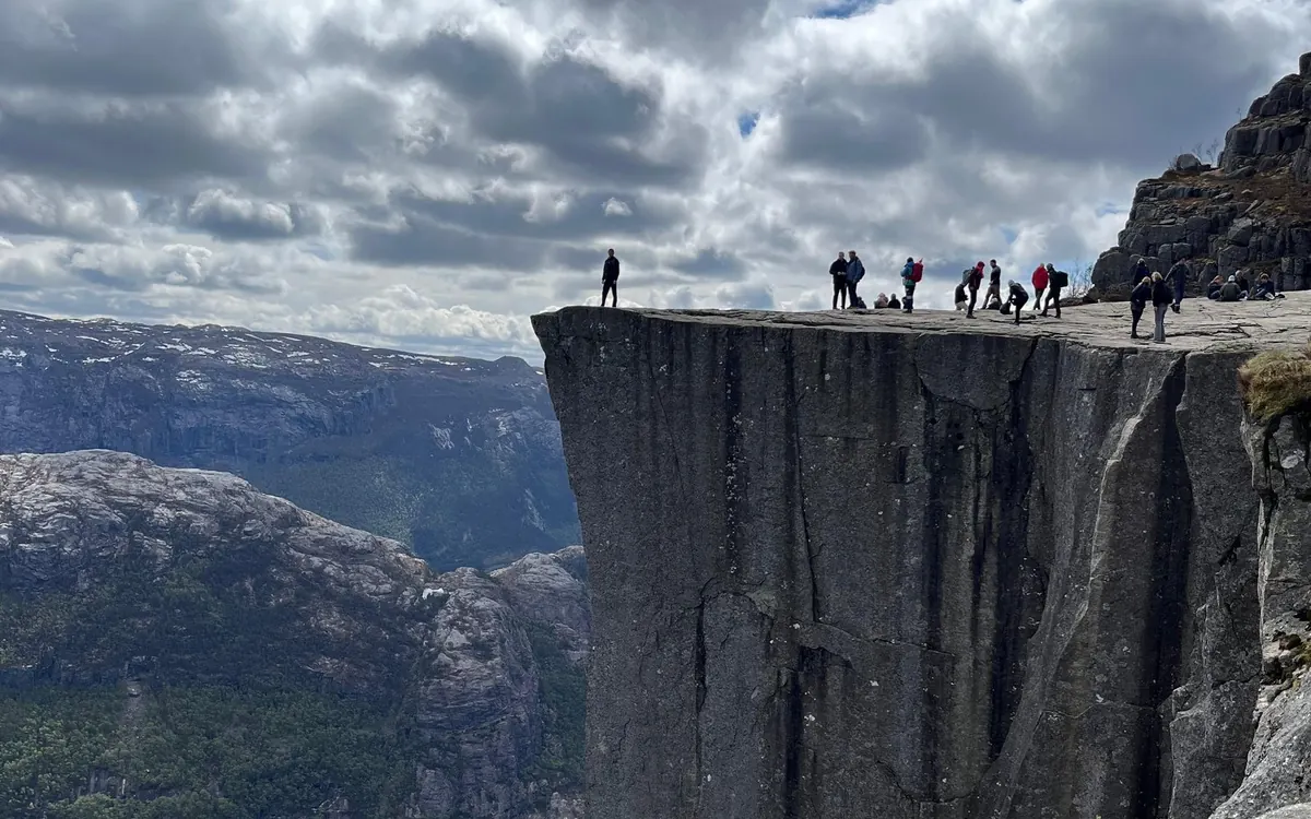 Hikers standing on the flat top of a sheer cliff above a fjord