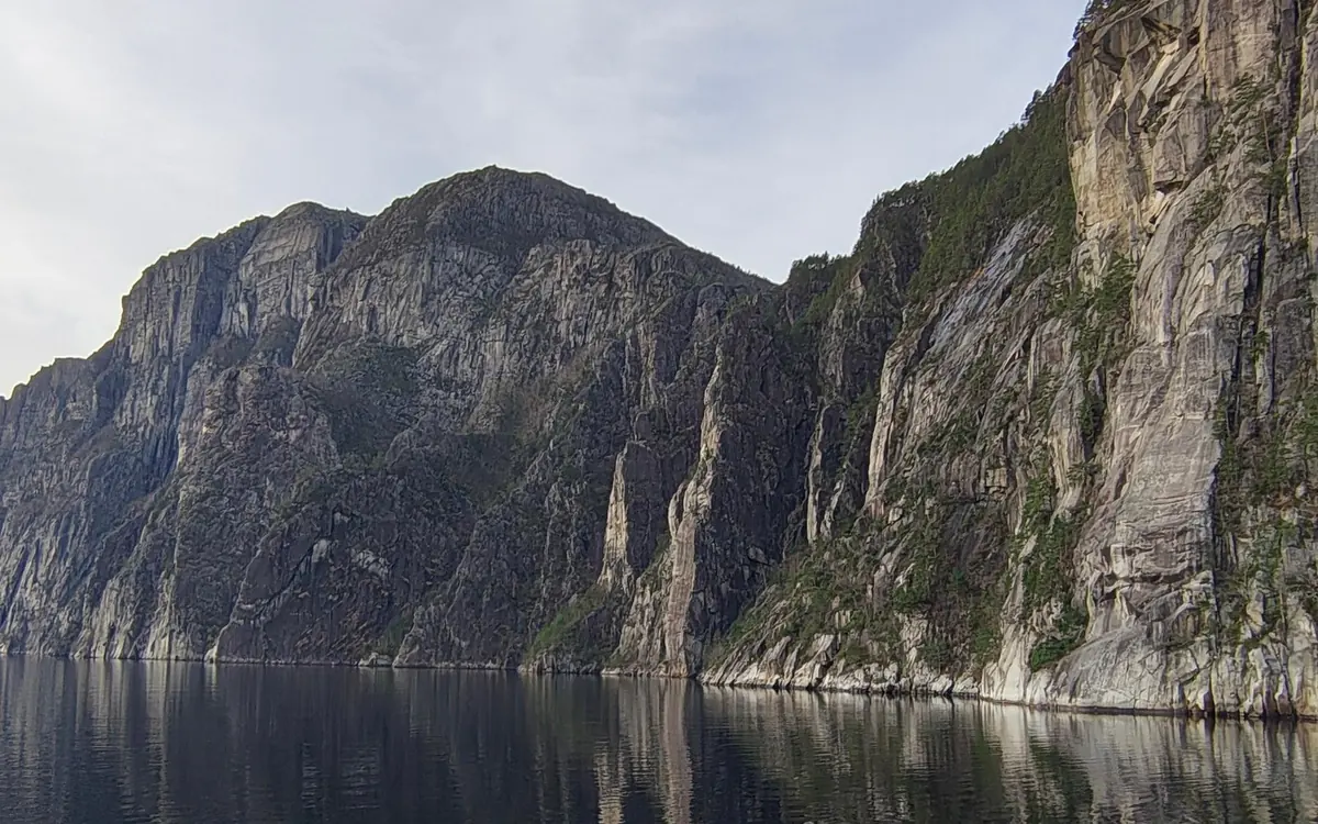 Grey cliffs rising straight out of still, dark fjord water
