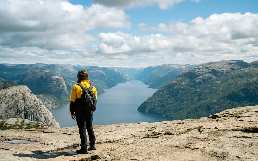 A hiker in a yellow jacket with a backpack looking over a fjord between hills