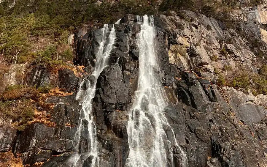 Two waterfalls pouring down a dark rock wall among autumn shrubs