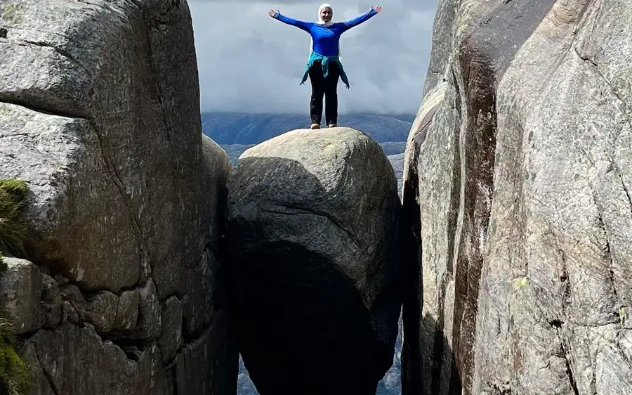 A hiker with arms raised on a boulder wedged between two rock walls