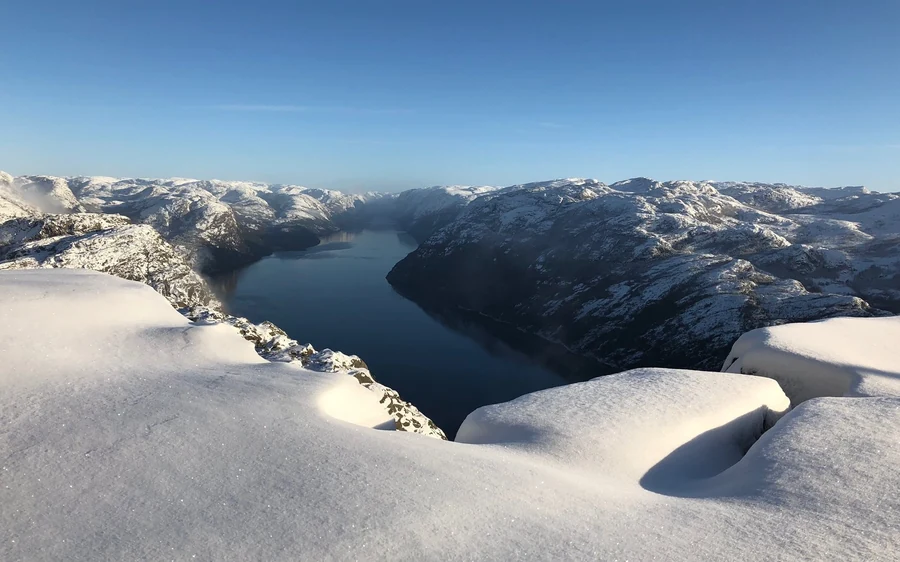 Deep snow on rounded rocks above a fjord, snowy hills beyond